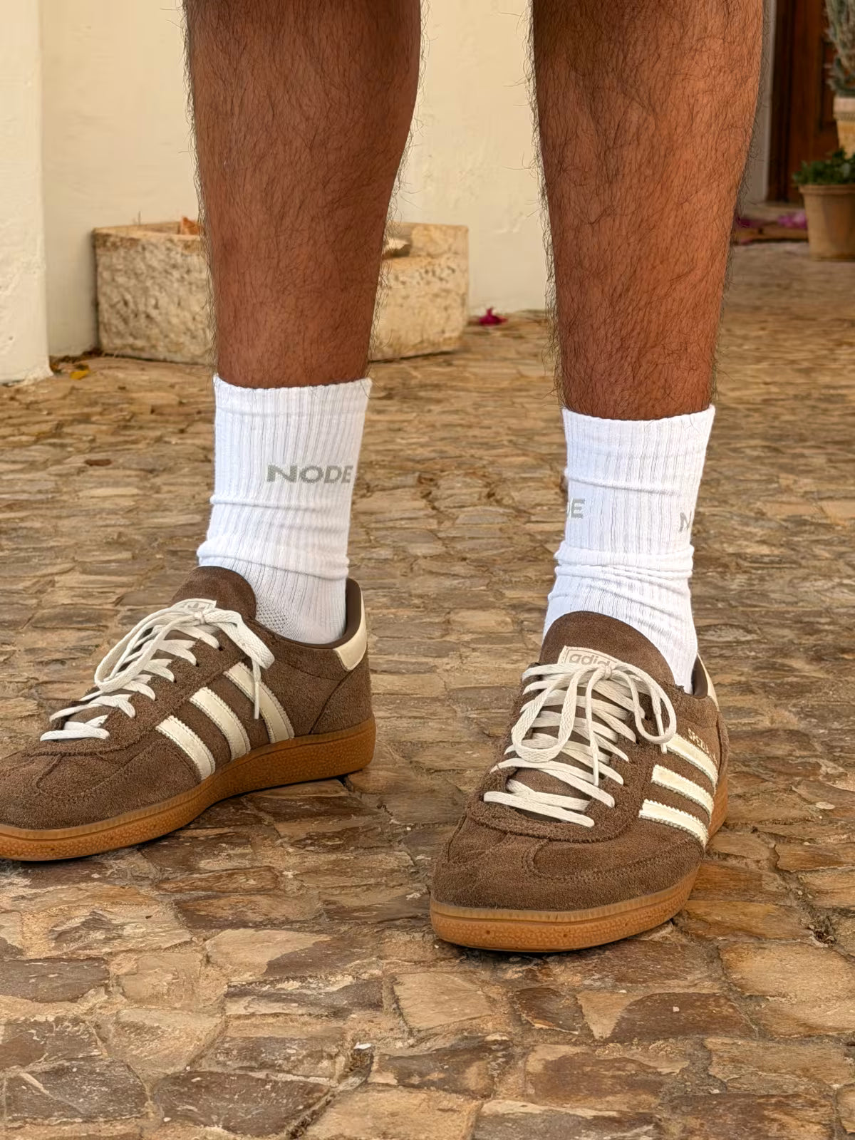 Brown Adidas sneakers with white socks with 'NODE' Branding on a stone pavement