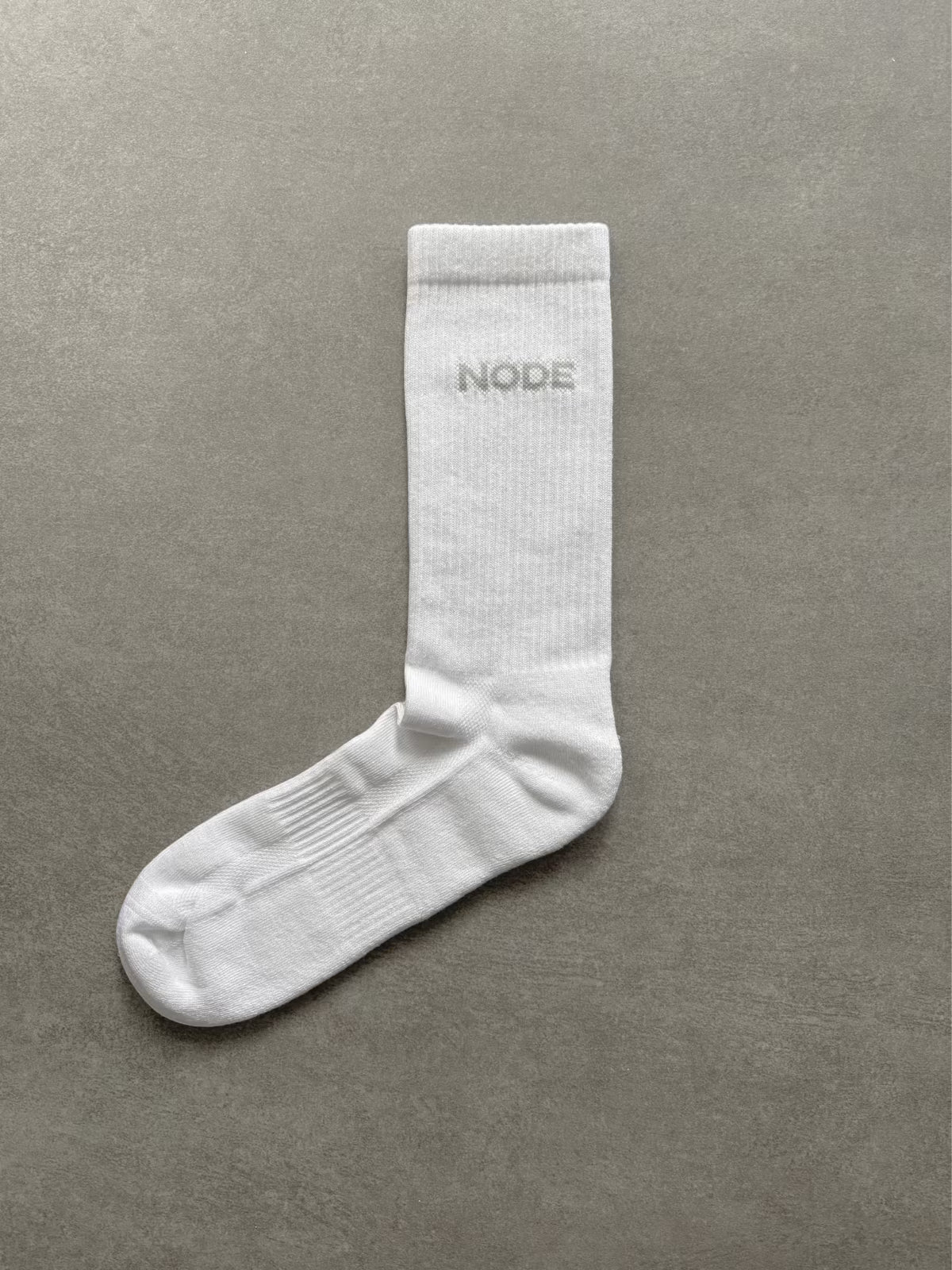 Product shot of white sock with 'NODE' branding on a grey background